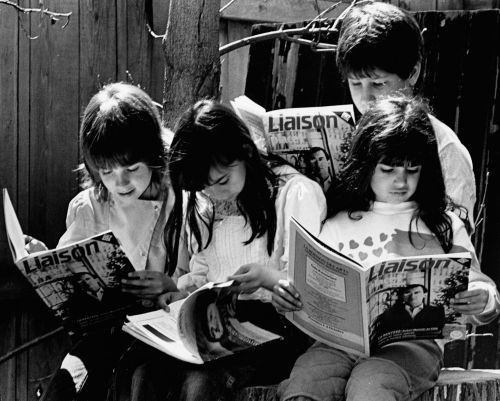 Photographie en noir et blanc d'enfants âgés entre 5 et 10 ans, absorbés dans la lecture du magazine Liaison. Trois fillettes sont assises. Un jeune garçon se tient debout derrière elles.