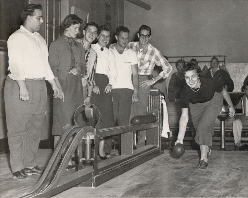 Black and white photograph of young adults playing bowling. They have fun.