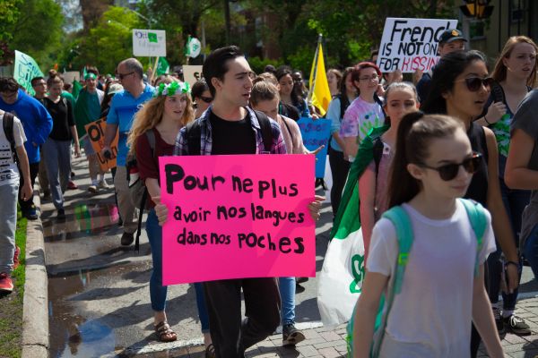 Photographie en couleur d'un groupe de manifestants, défilant dans la rue. Plusieurs portent les couleurs du drapeau franco-ontarien. L'un d'entre eux tient une pancarte affichant le slogan: Pour ne plus avoir nos langues dans nos poches.