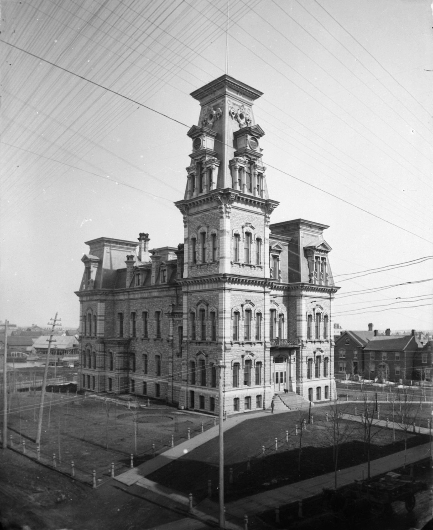 Black and white photograph of a four-storey stone building, dominated by a large tower on its right corner. The building is separated from the neighbouring houses by a park. Diagonal lines are visible at the top of the image.