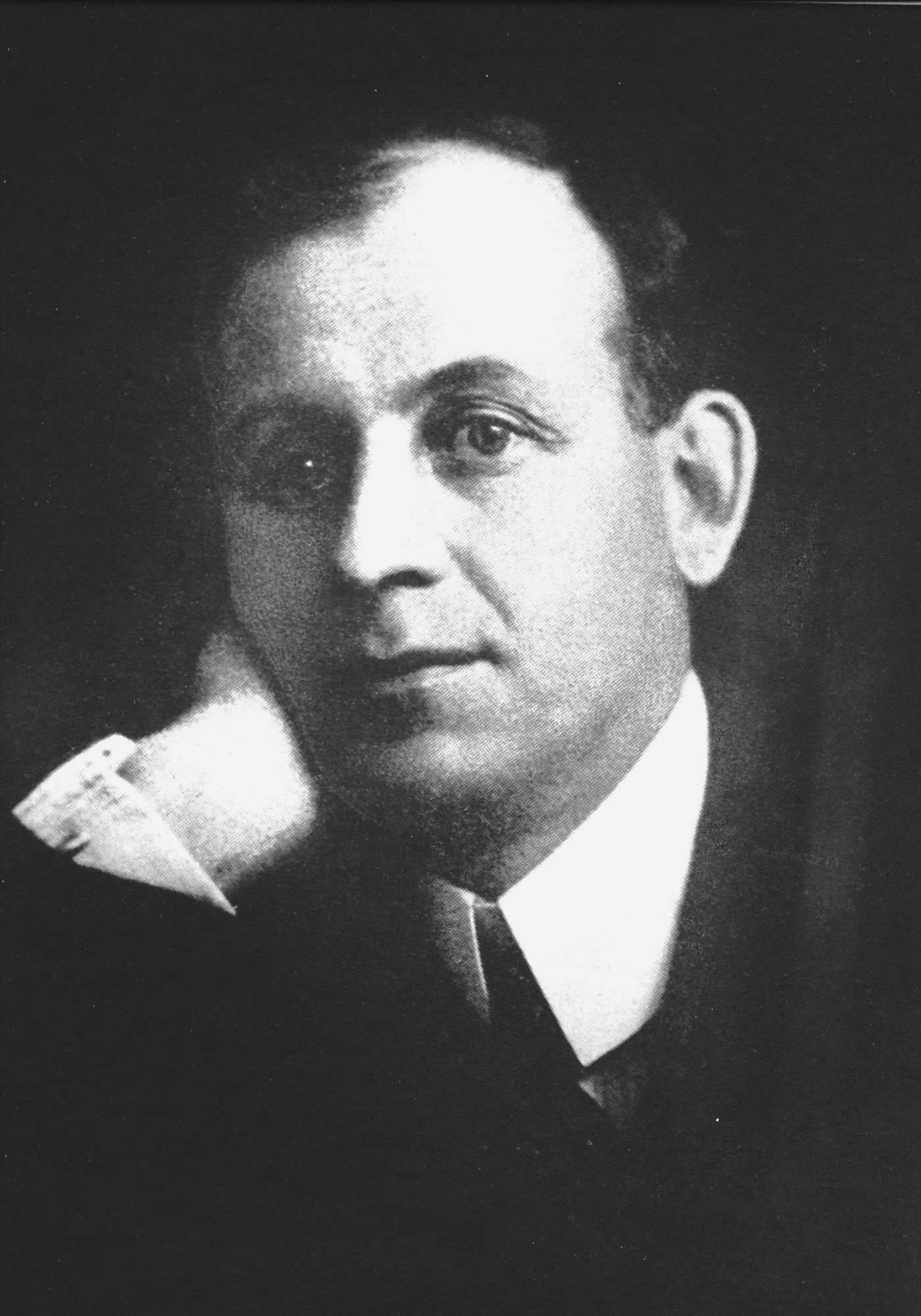 Black and white studio photograph of a middle-aged man in a suit. He sits with his head leaning against his right hand. He seems absorbed in his thoughts.