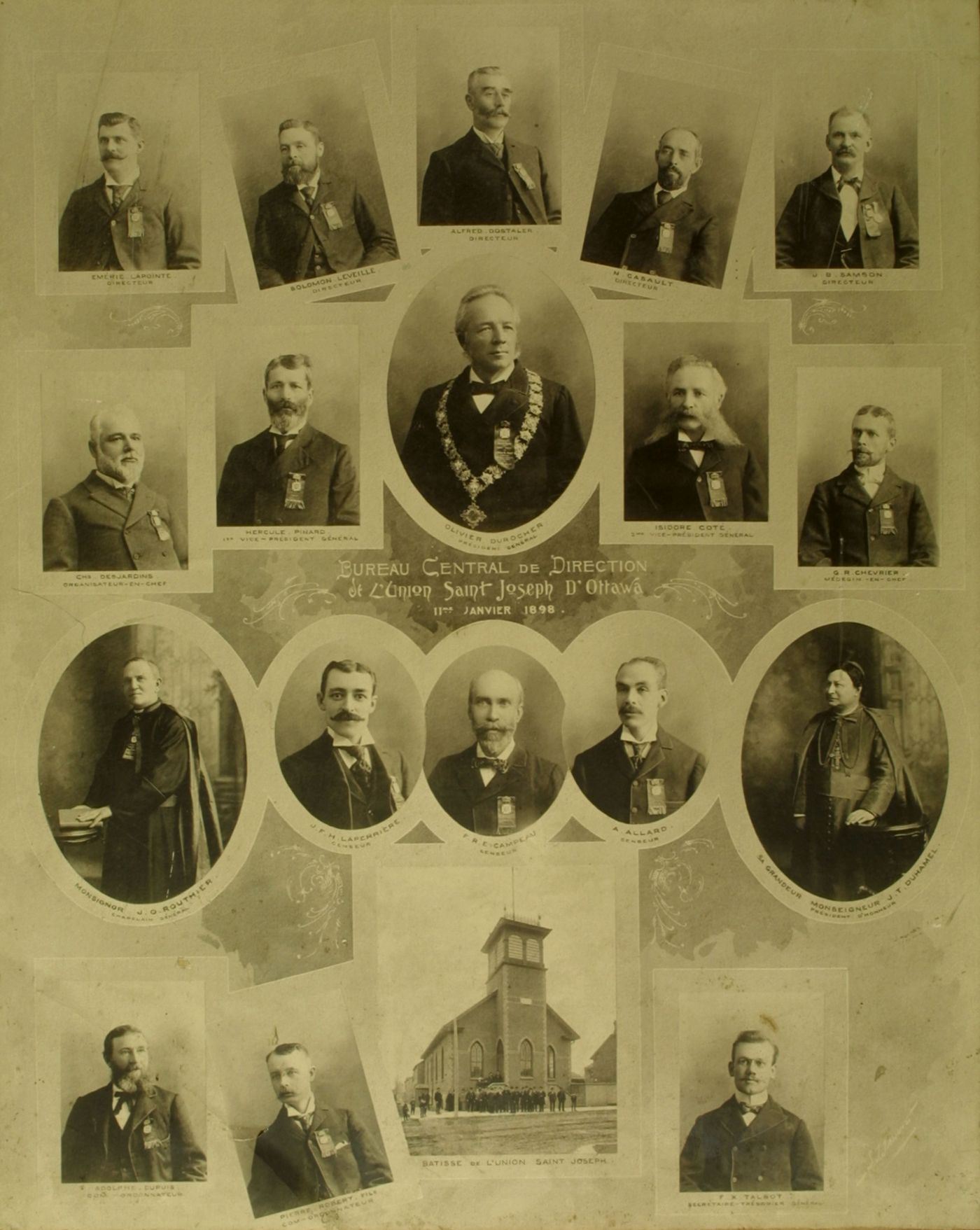 Display board with 18 black and white photographs, depicting men in suits and ties, with the exception of two clerics. Names and titles appear below the photographs. The man in the middle picture wears  the Mayor’s chain of office. A picture of a two-storey building with large front tower is included, as well as a caption in French.