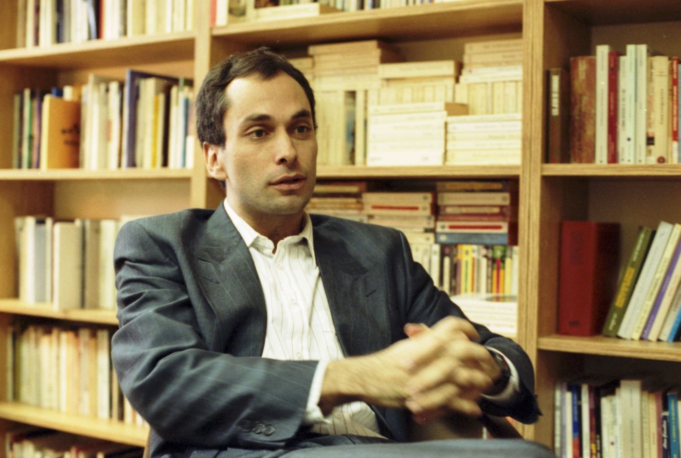 Photographie en couleur d’un homme d’âge moyen, vu de trois quarts. Il est assis, les mains jointes devant lui. Il a les cheveux bruns et la peau basanée. Il porte un costume sans cravate. À l’arrière-plan, une bibliothèque.