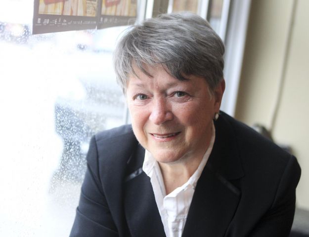 Photographie en couleur d’une femme d’âge mûr, portant un chemisier blanc et une veste noir. Elle sourit à la caméra. L'arrière-plan est flou.