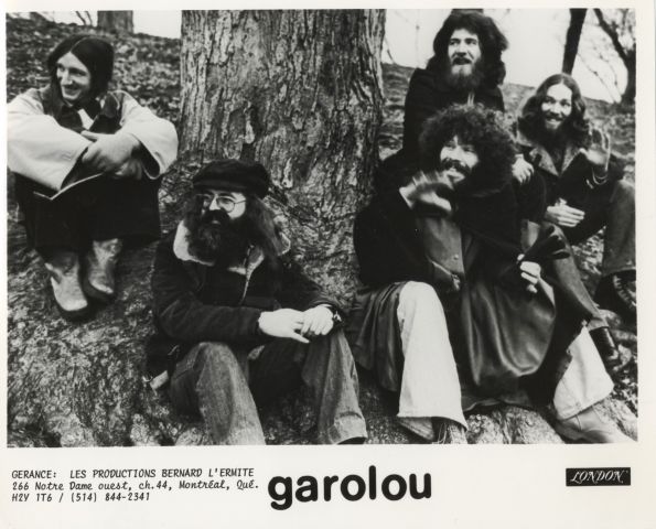 Black and white photograph with text printed in French. Five long-haired young men sit at the foot of a large tree. They wear coats and casual clothes. At the bottom of the photo, the name of the group and management information.